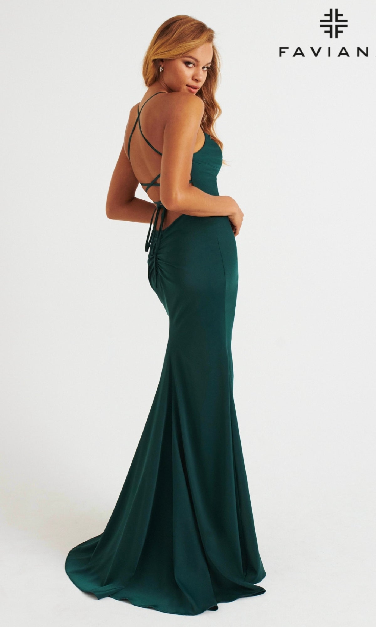 A woman models the Faviana Lace-Up-Back Long Prom Dress 11064 in dark green, featuring a fitted, floor-length design and strappy open back. The Faviana logo appears in the top right corner on a plain white background.